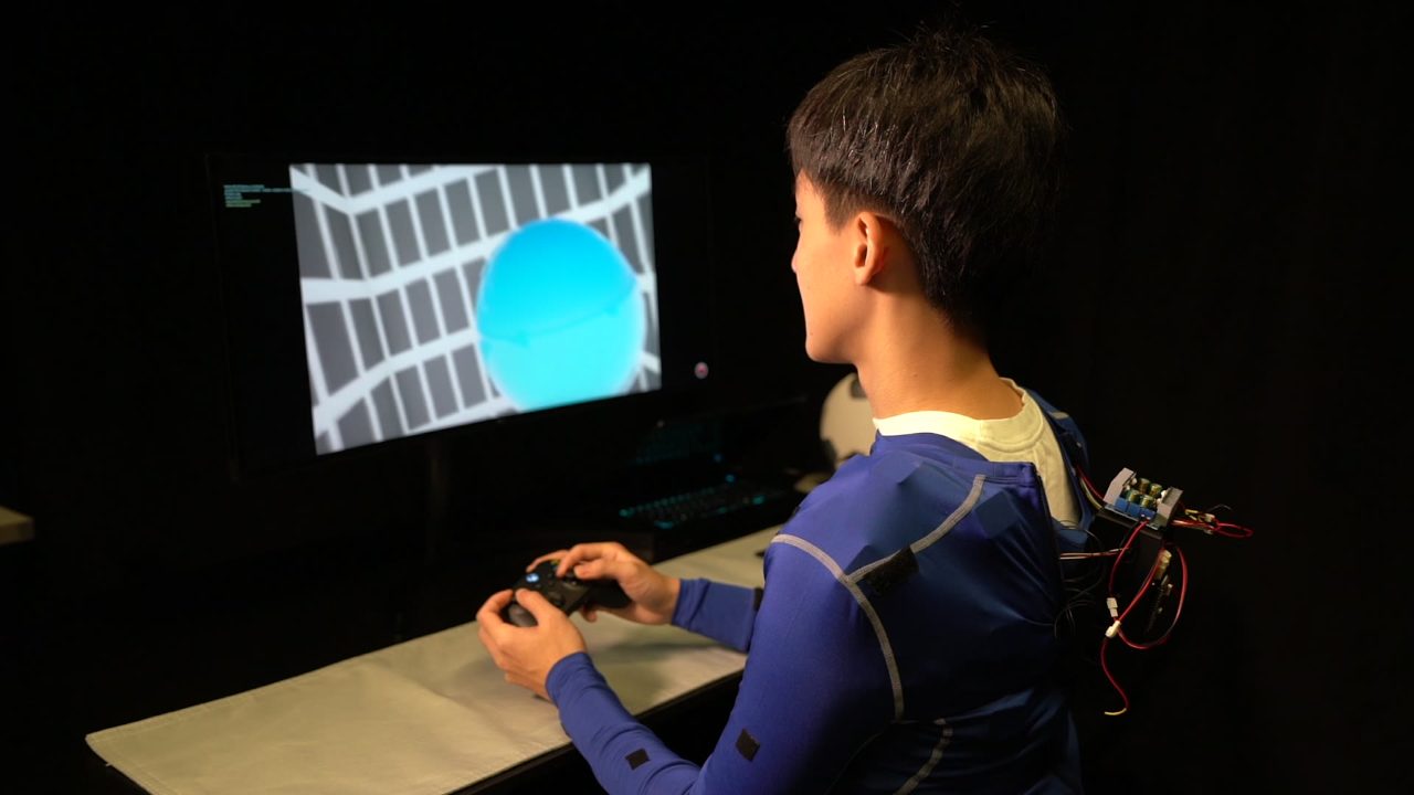 Participant in the suit flying the simulated drone at a desk